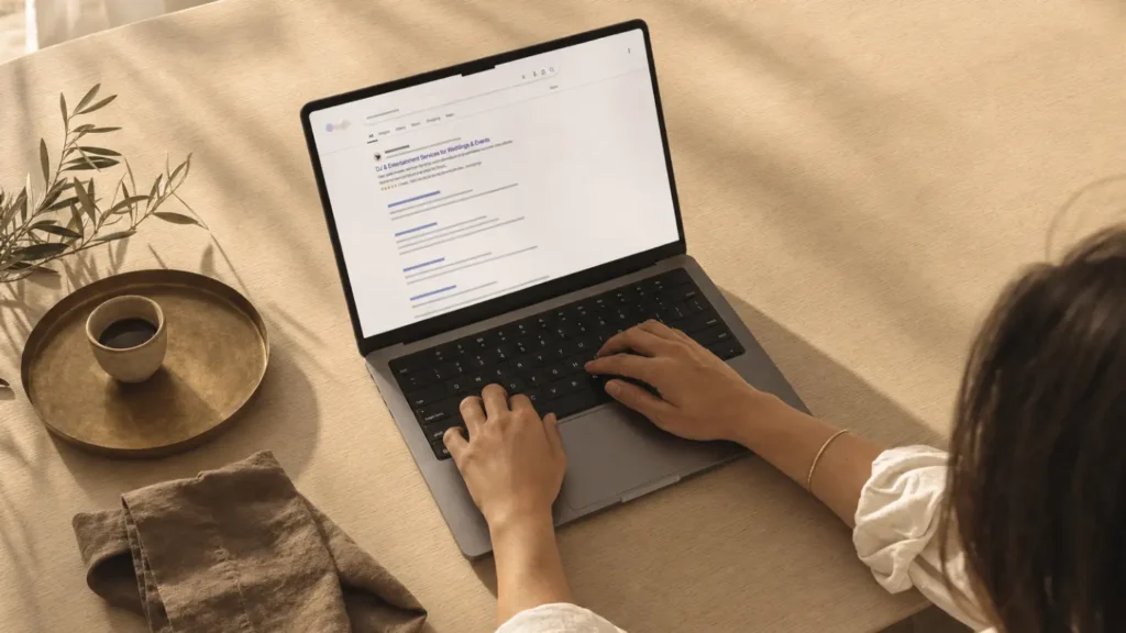Woman at a warm editorial desk workspace viewing a Google search results page showing a DJ and entertainment company ranking at the top